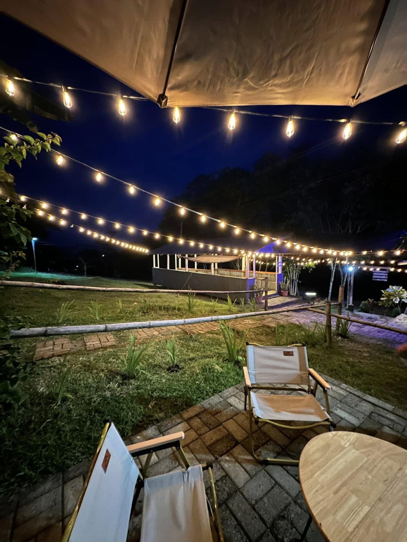 The lawn at Lawagon after dark, criss-crossed by strings of warm bulbs, with folding chairs and a low wooden table in the foreground